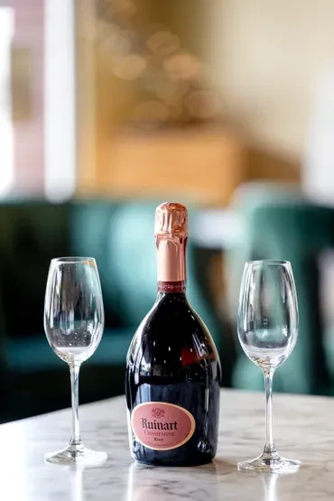 Ruinart Champagne Rosé bottle and two glasses on marble table.