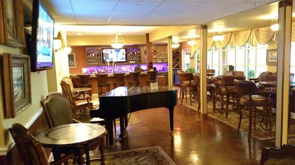 Warmly lit restaurant bar, dining area, and central black grand piano.