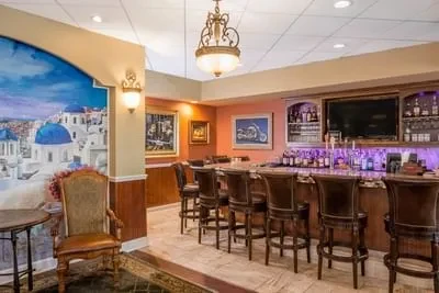 Restaurant bar area with purple-lit bottles, TV, stools, and island mural.
