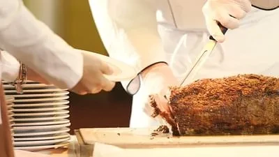 Chef carving roasted meat at a professional food service station.