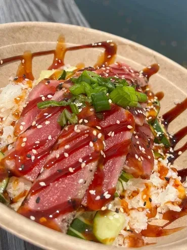 Seared tuna rice bowl with sauce, sesame seeds, and green onions.