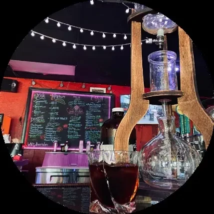 Multi-level glass and wood beverage apparatus, two dark drinks, dim bar.