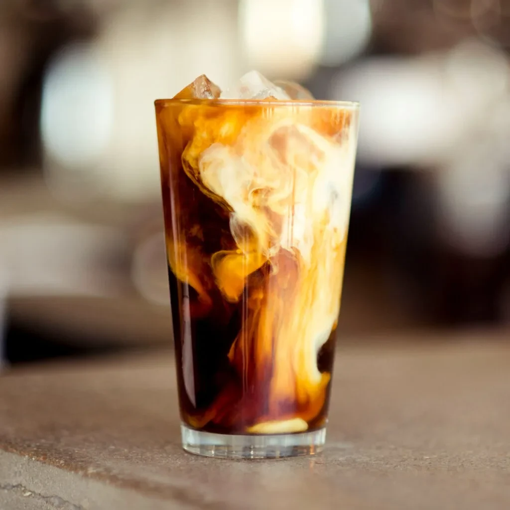 Tall glass of iced coffee with swirling cream and ice.