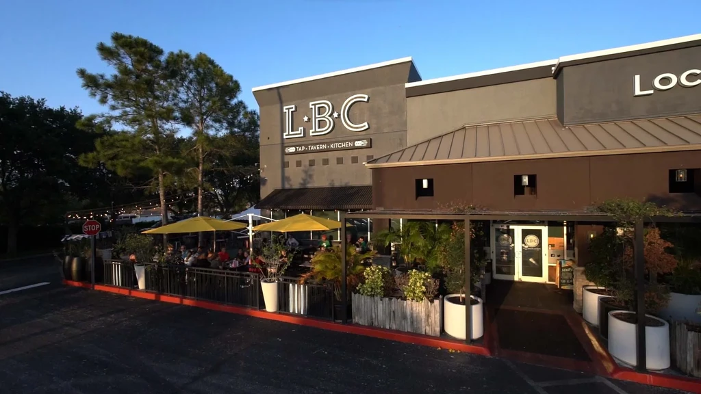 LBC TAP restaurant exterior, warm patio lighting, yellow umbrellas, seated patrons.
