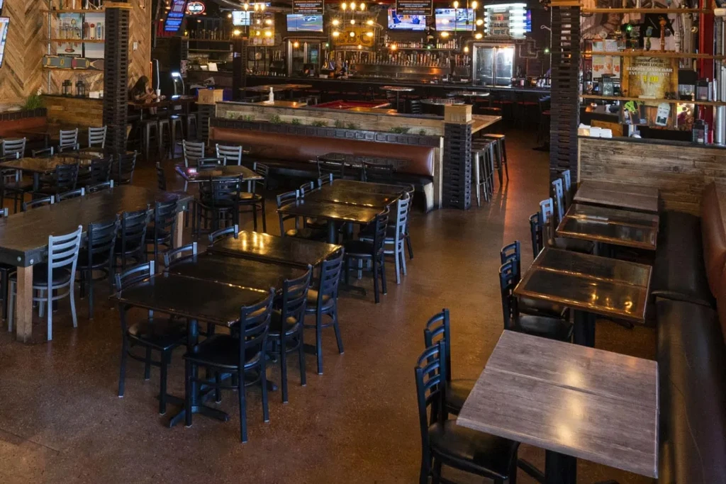 Casual restaurant interior with dark tables, a long bar, and warm lighting.