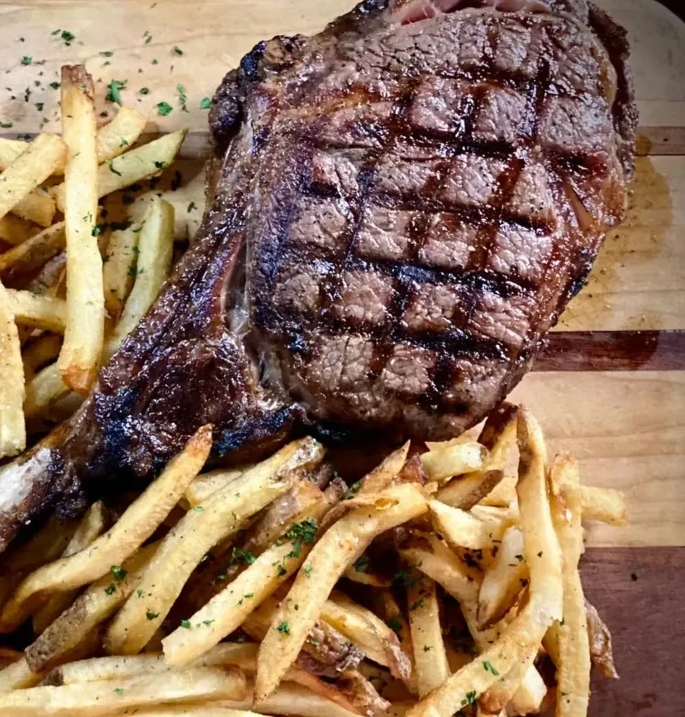 Juicy grilled ribeye steak with crispy fries on a wooden board.