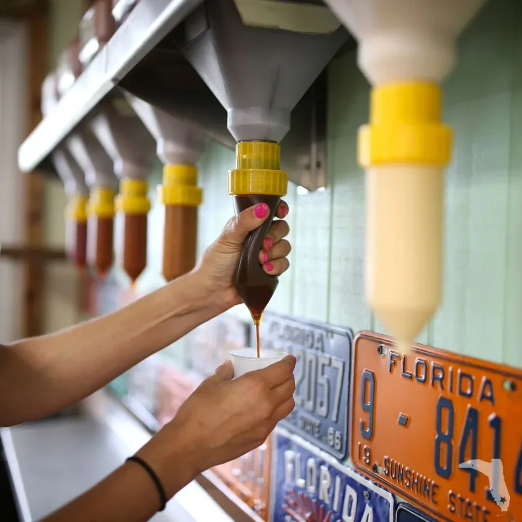 Close-up of hands dispensing dark sauce from a self-serve restaurant dispenser.