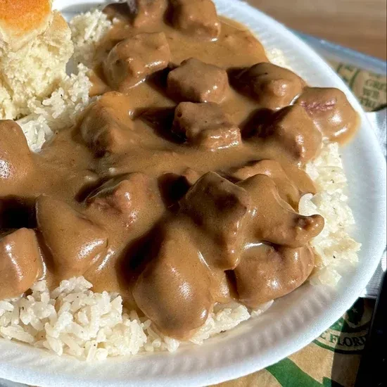 Close-up: Rice, cubed meat in gravy, with a biscuit on a plate.