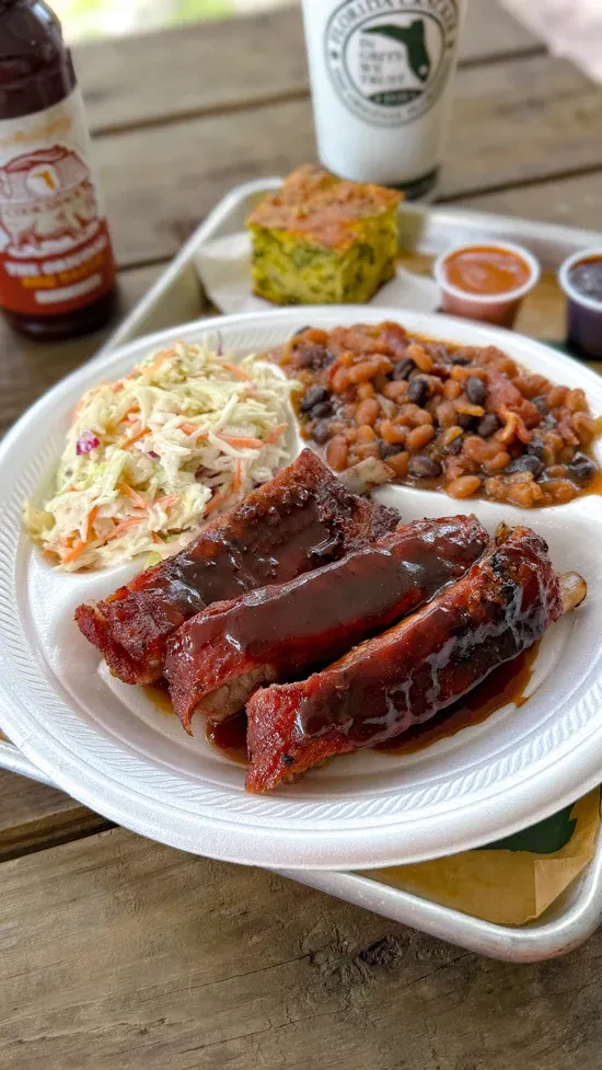 BBQ ribs, coleslaw, and baked beans on a white styrofoam plate.