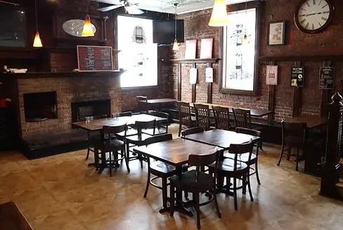 Rustic empty restaurant interior with brick walls, wooden furniture, and chalkboard.