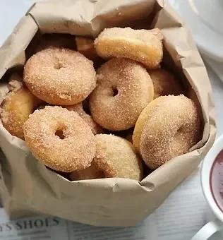 Sugar-coated mini donuts in brown paper bag, with coffee and newspaper.