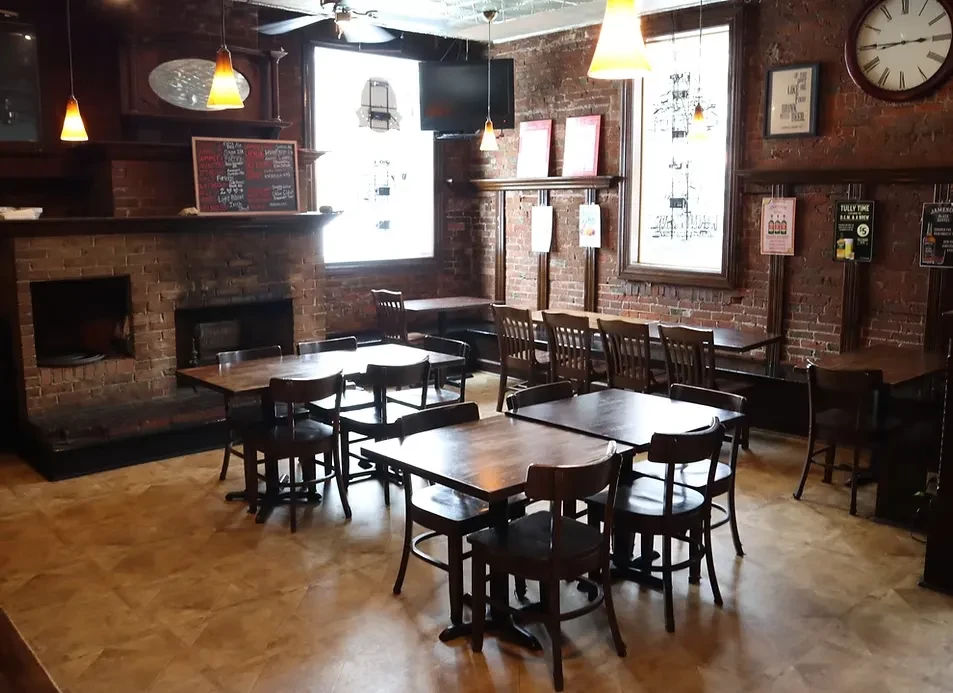 Rustic empty restaurant interior with brick walls and wooden furnishings.