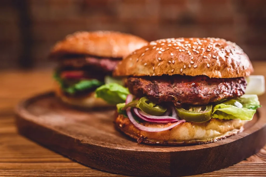 Two gourmet burgers with jalapeños on a wooden board.