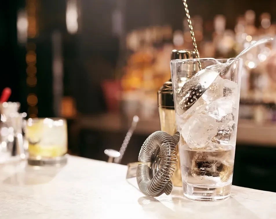 Bartending tools, ice, and a drink being made on a bar counter.