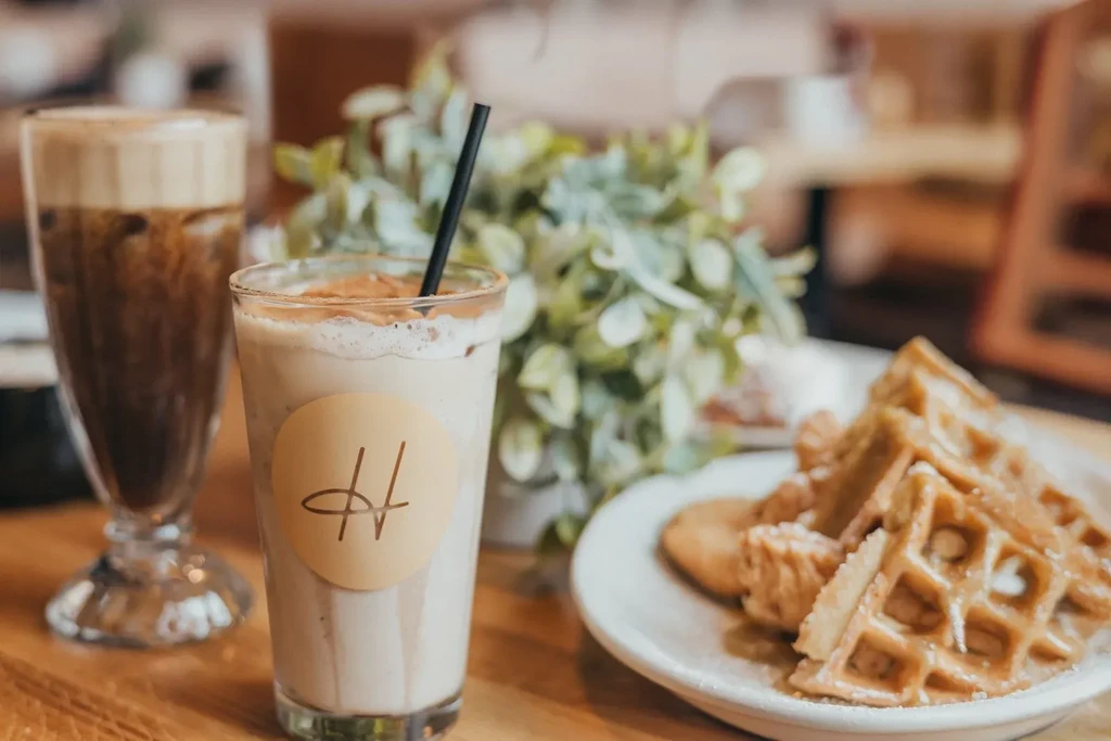 Creamy drink, iced coffee, powdered waffles, and pastries on a cafe table.