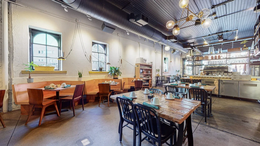 Empty modern industrial restaurant dining room with set tables and open kitchen.