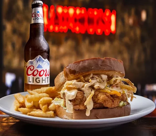 Well-stacked fried chicken sandwich, crinkle-cut fries, Coors Light bottle.