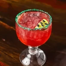 Vibrant red cocktail with green rim and fruit garnish.