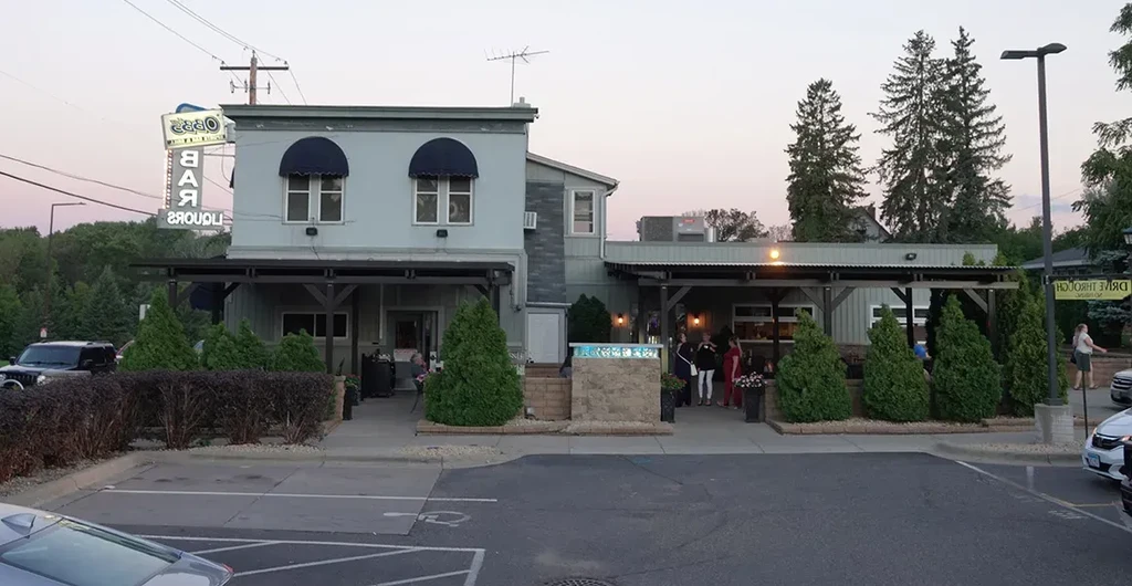 Two-story bar and liquor store with a neon sign at dusk.