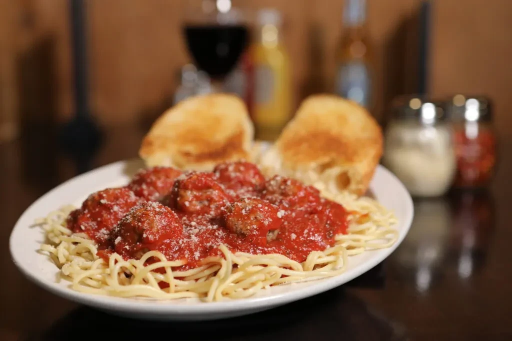Spaghetti and meatballs with cheese and toasted bread on a dark table.