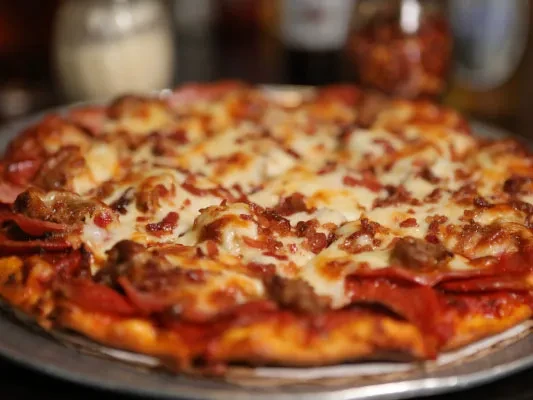Close-up of bubbly, golden-brown pizza with pepperoni, sausage, and bacon.