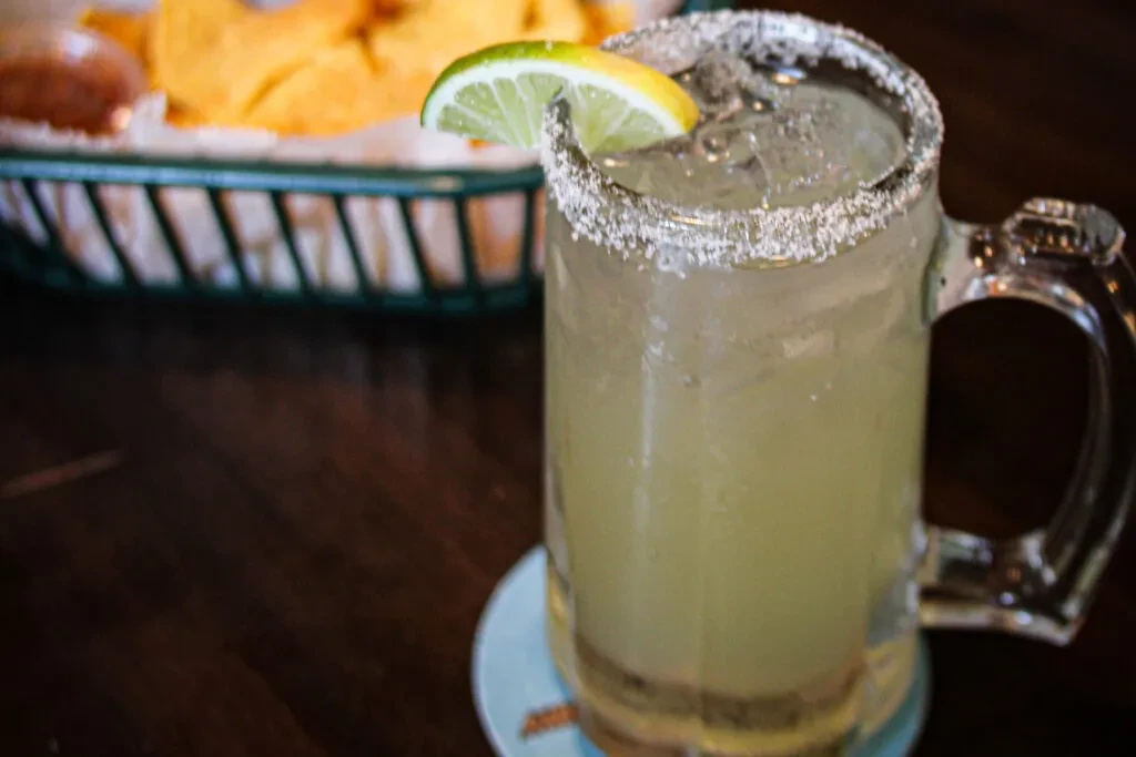 Pale green margarita with salted rim, lime, ice, chips, and dip.