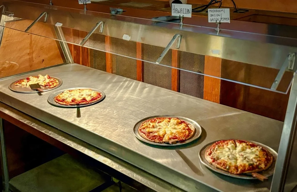 Buffet-style counter with various labeled pizzas behind a sneeze guard.