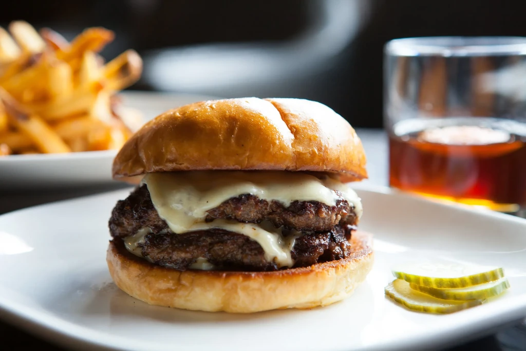 Double cheeseburger with melted cheese, pickles, fries, and a beverage.