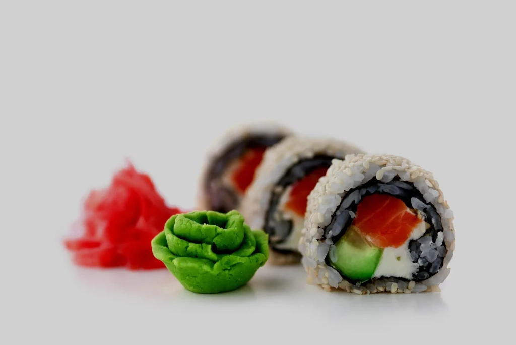 Three sushi rolls with salmon, avocado, wasabi, and ginger.