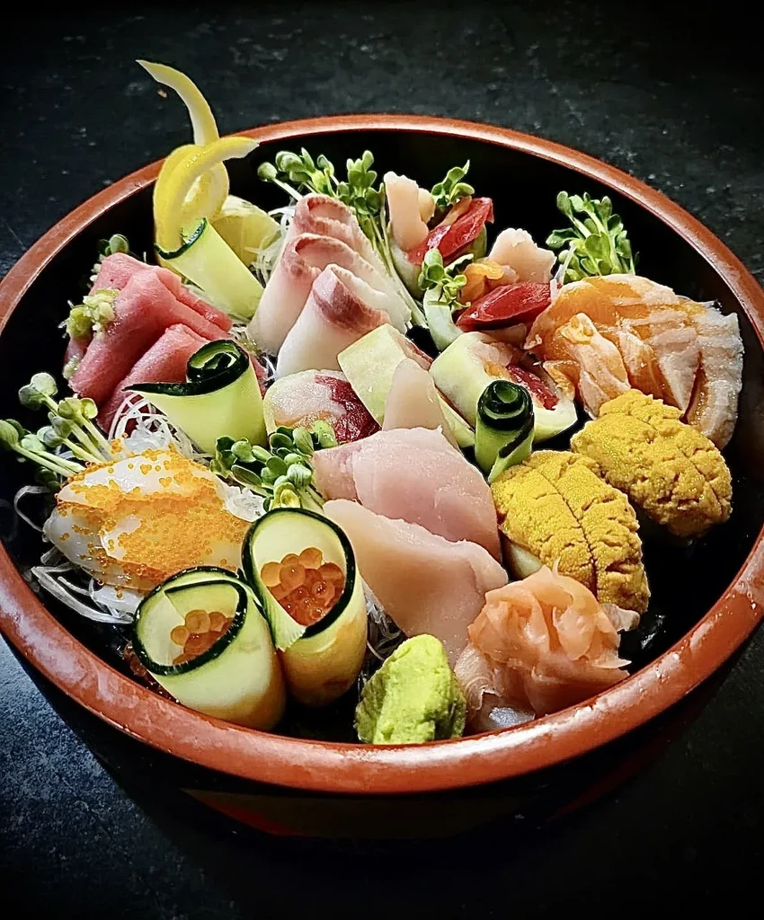 Close-up of a dark bowl with assorted sashimi, uni, and roe.