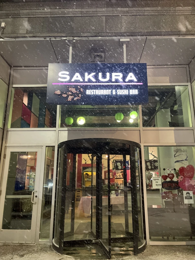 Exterior of Sakura Restaurant & Sushi Bar during heavy snowfall at night.