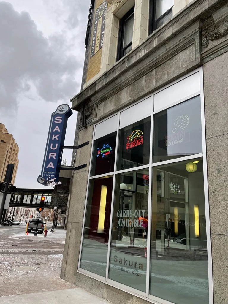 Snowy exterior of Sakura Restaurant & Bar with prominent blue neon sign.