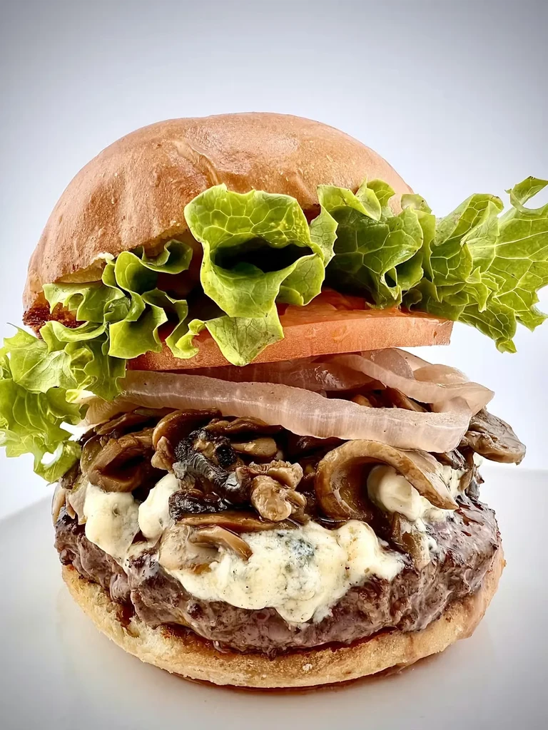 Close-up, stacked gourmet burger with blue cheese and mushrooms.