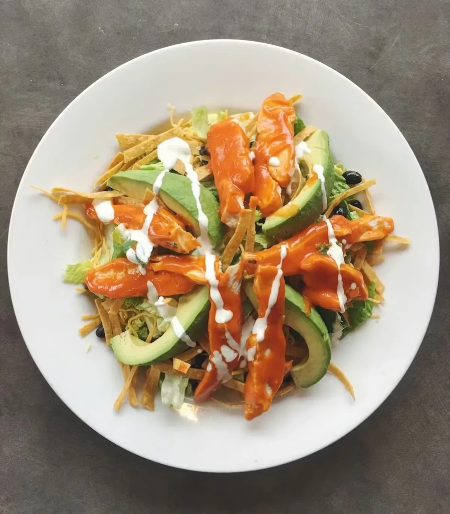 Overhead salad with lettuce, avocado, chicken, beans, tortilla strips, dressing.
