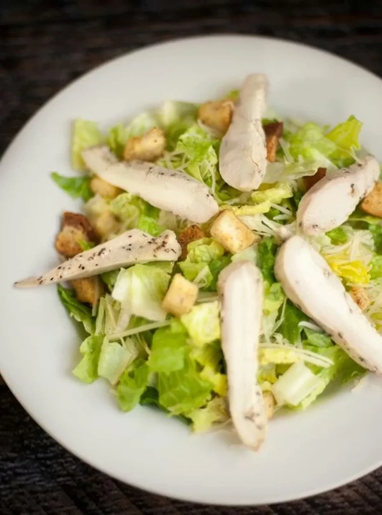 Caesar salad with chicken, croutons, and cheese on a white plate.