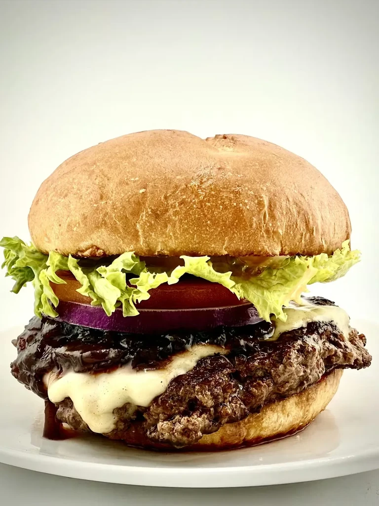 Stacked gourmet burger with grilled patty, melted cheese, and fresh vegetables.