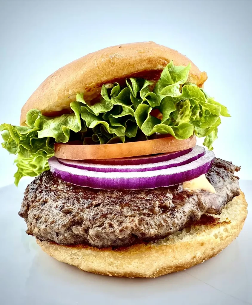 Close-up of a gourmet beef burger with cheese, lettuce, tomato, onion.