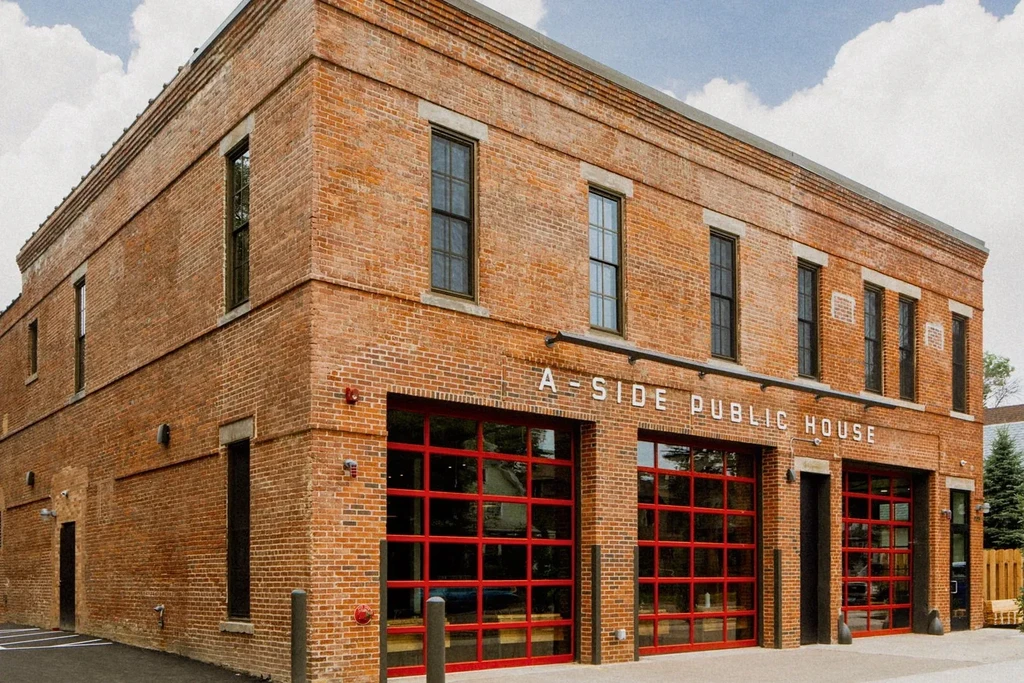 Two-story brick A-SIDE PUBLIC HOUSE with red garage-door windows.