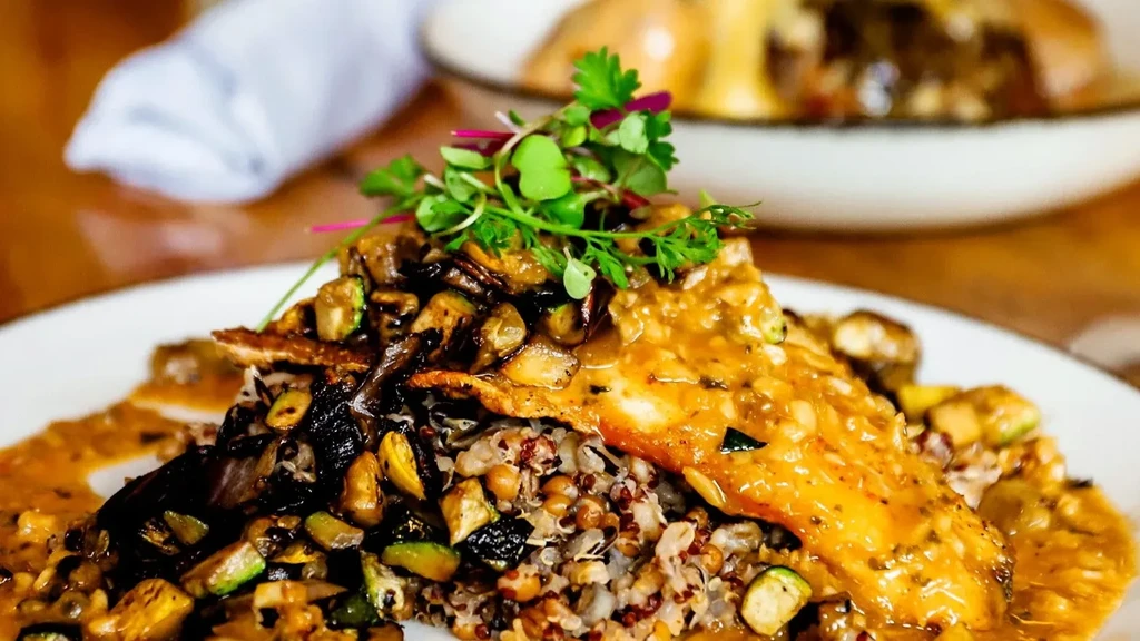A plated fish dish with golden sauce, grains, vegetables, and microgreens.
