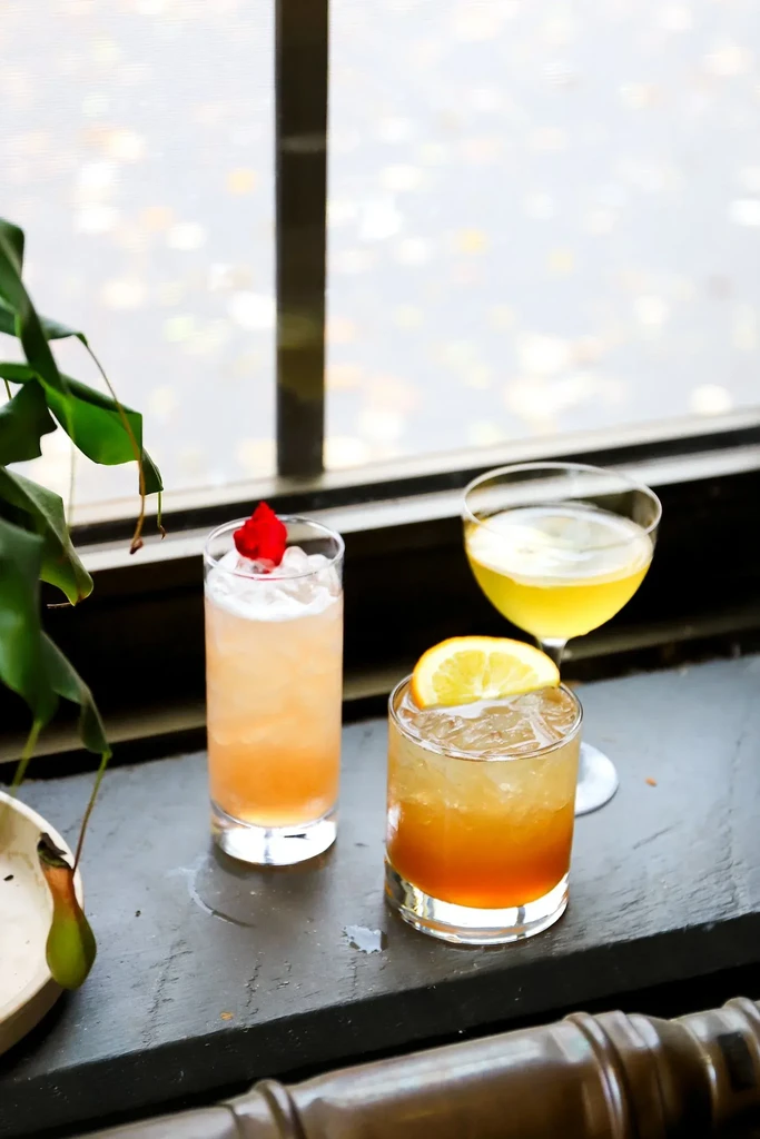 Three different cocktails on a dark windowsill with blurred urban background.