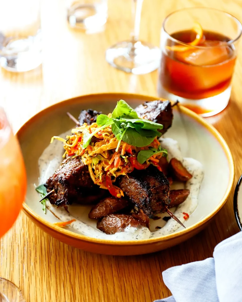 Grilled meat skewers with potatoes, sauce, and a cocktail.