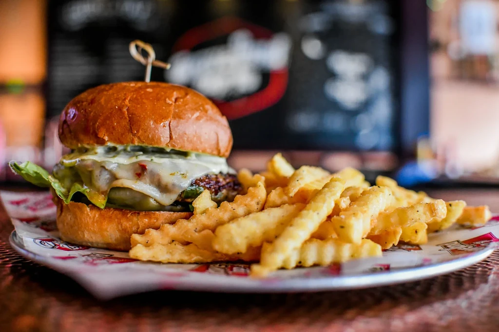 Close-up of a burger with melted cheese and seasoned crinkle-cut fries.