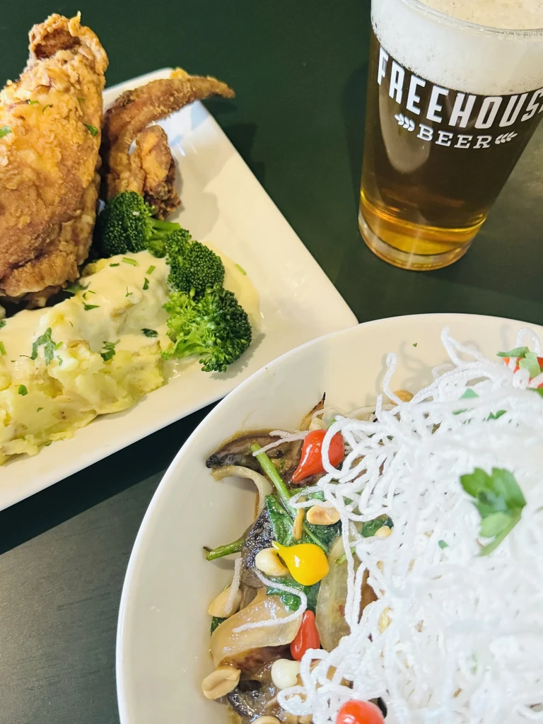 Overhead view: fried chicken, beer, and a vegetable noodle dish.