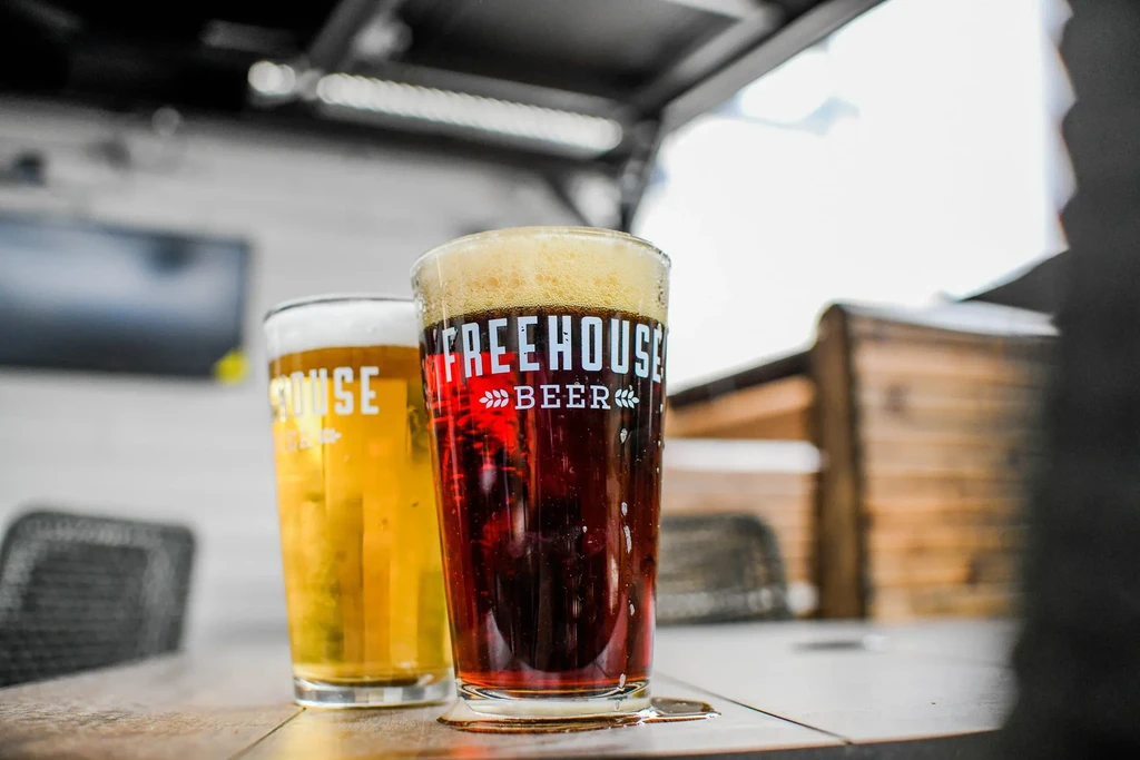 Two glasses of frothy beer: dark "FREEHOUSE BEER" and a golden beer.