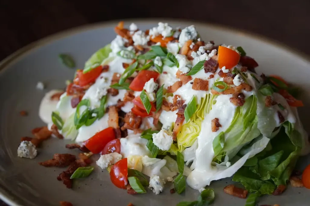 Wedge salad with creamy dressing, tomatoes, blue cheese, bacon, green onions.