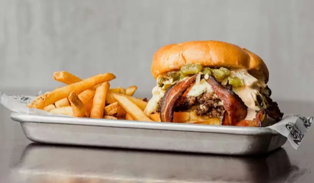 Bacon cheeseburger with chilies and golden fries on a tray.