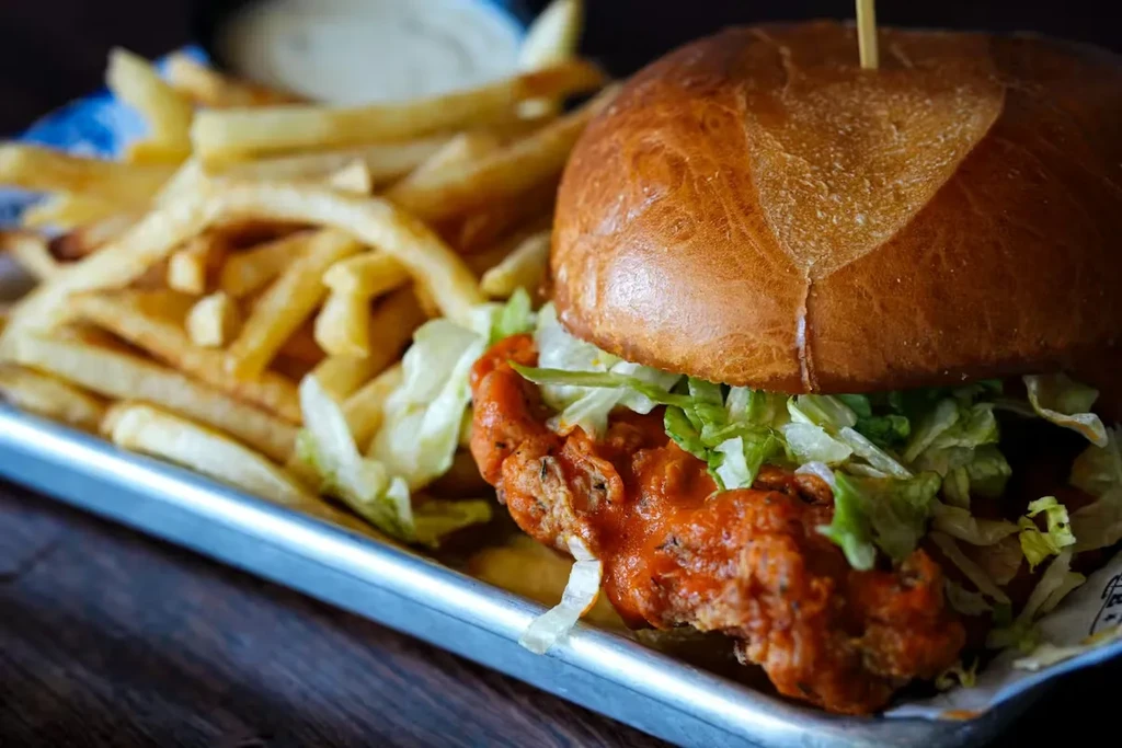 Close-up chicken sandwich, fries, and dipping sauce on a metal tray.