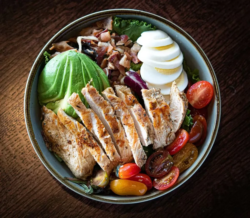 Overhead view of chicken, avocado, egg, bacon, and tomato power bowl.