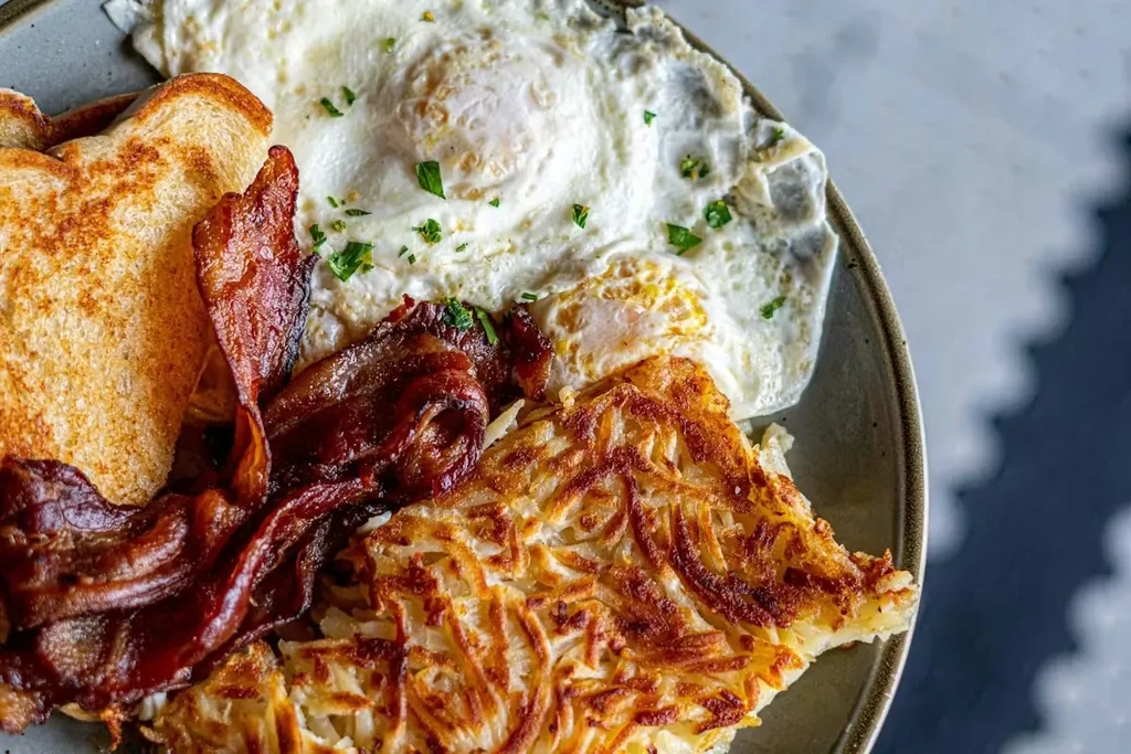 Breakfast plate with herbed eggs, crispy bacon, hash browns, and toast.