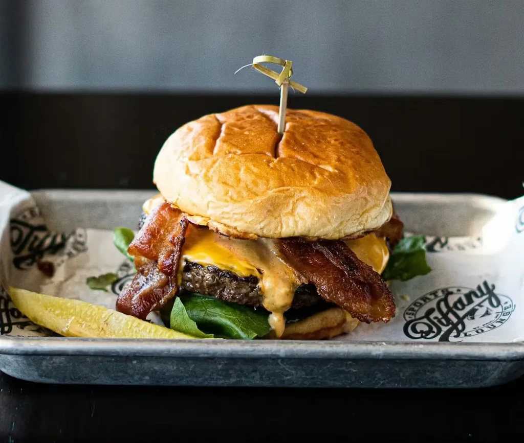 Large burger with bacon, melted cheese, lettuce, and a pickle spear.